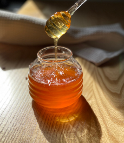 Honey spoon being dipped into honey jar